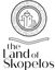 Black and white logo for 'the Land of Skopelos' featuring a circular emblem with a church illustration and wood-grain texture, above stylized text.
